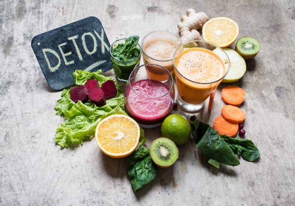 a group of bright-colored vegetable and fruit juices next to a sign reading “detox.”