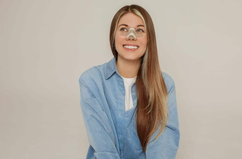 A smiling young woman with a nasal cast after rhinoplasty.