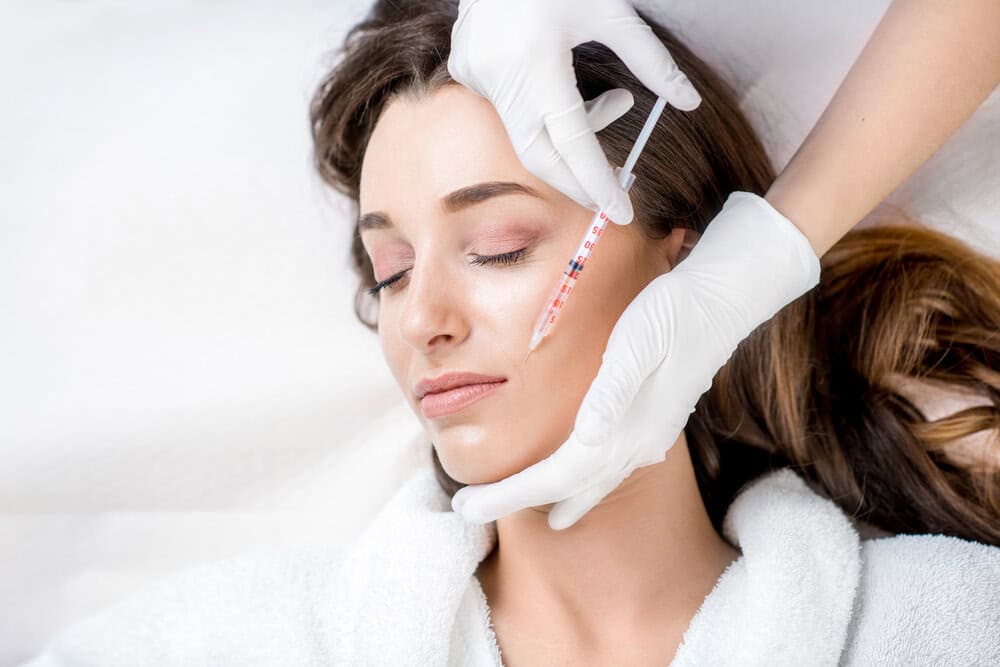 a young woman receives a botox injection from a doctor in white gloves