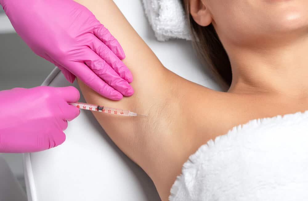 A doctor in pink gloves administers armpit botox to a female patient