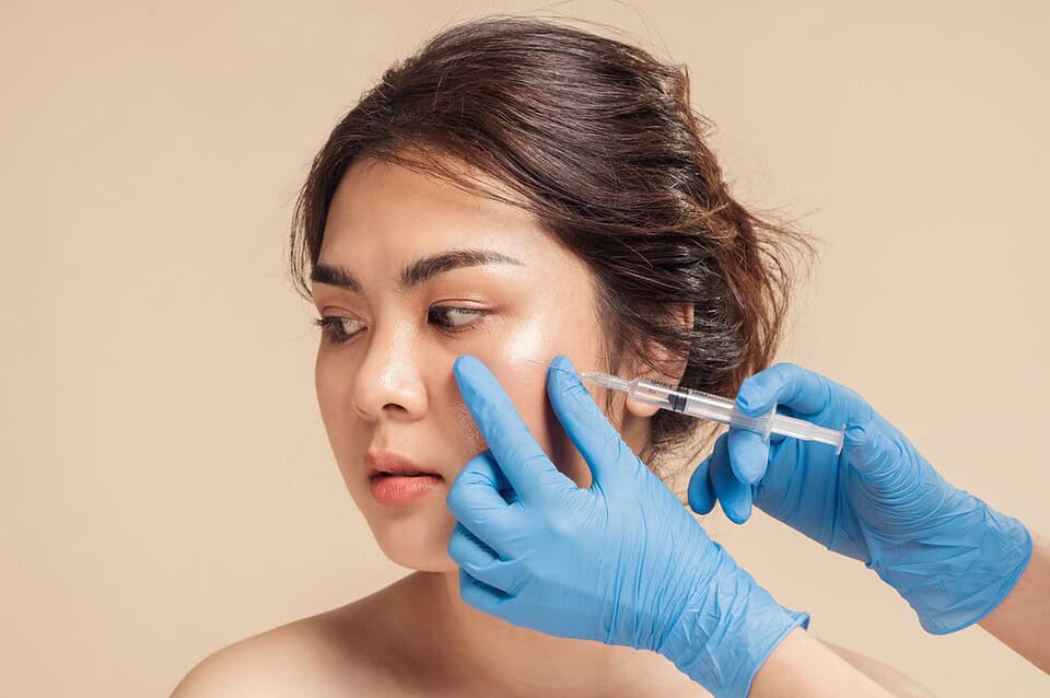 A young Asian woman receives an injection of filler into her cheek