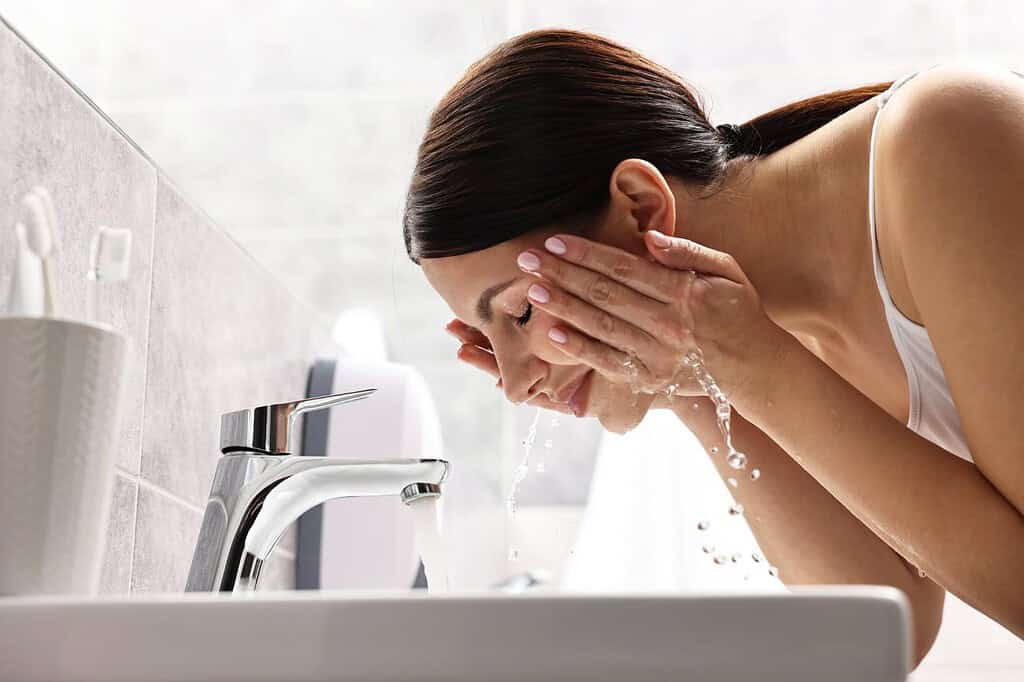 A woman cleansing her face at a sink 