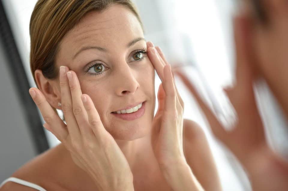 A woman looking for facial wrinkles in the mirror