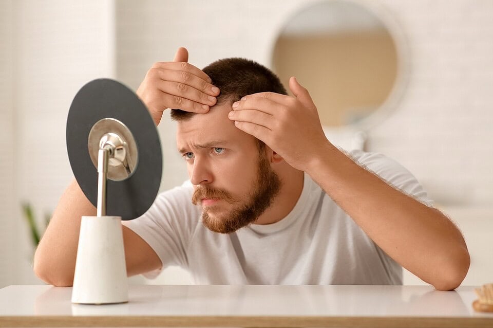 A man checks his hair in a mirror, wondering how many hair grafts are needed for a hair transplant.