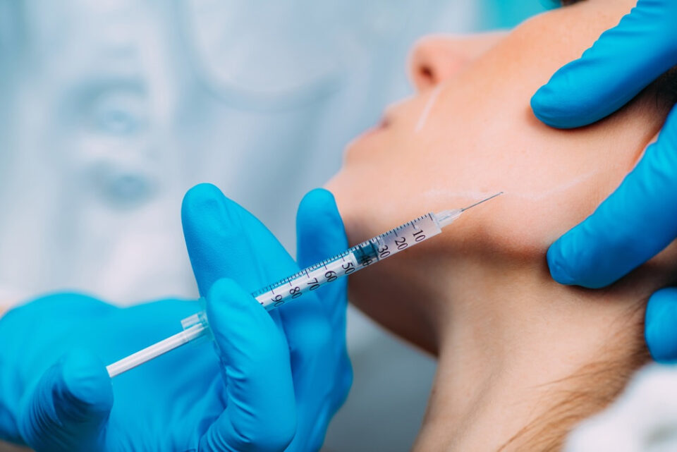 Clinician performing a jawline filler injection along the jaw of a female patient