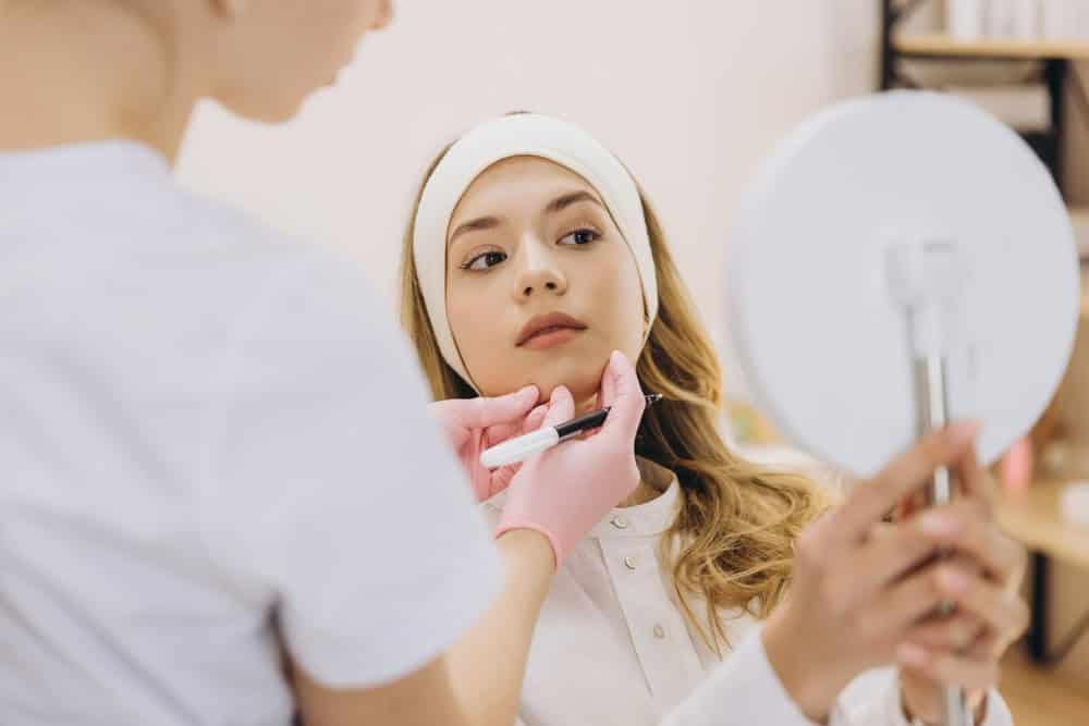Practitioner marking jawline filler injection sites as the client views in a mirror