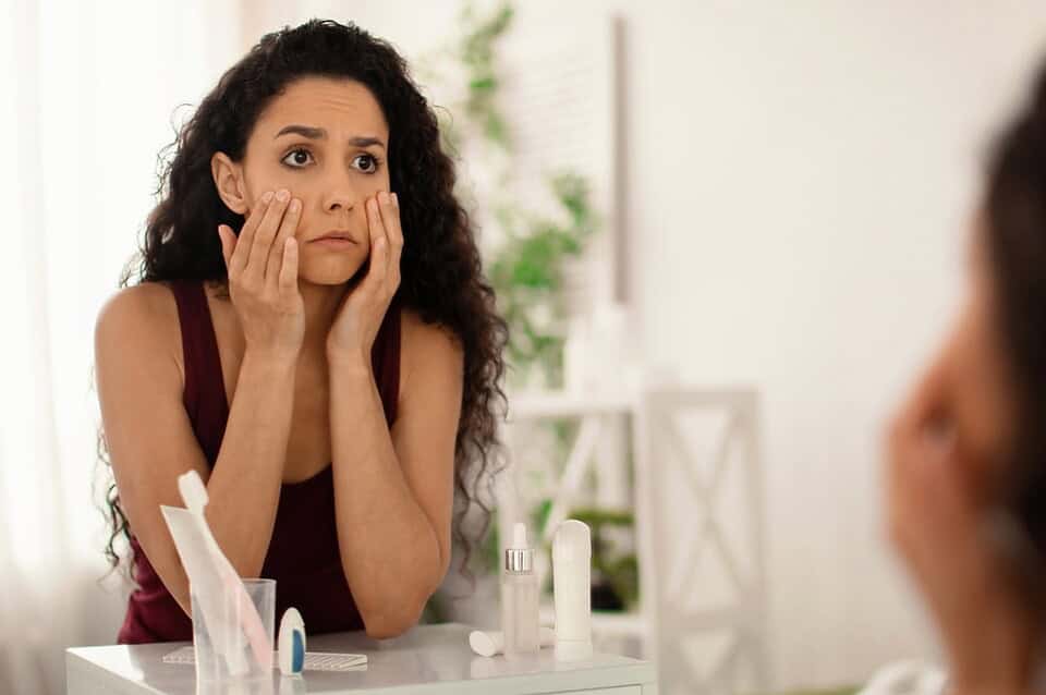 Woman with curly hair noticing sunken under-eyes while reviewing her skincare routine