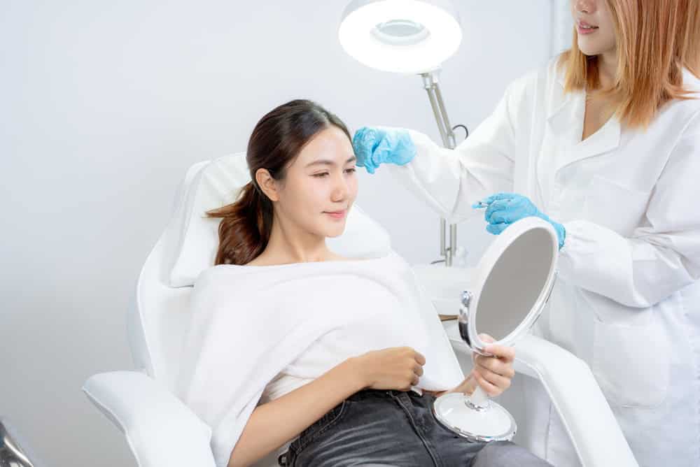 A woman holding a mirror before her forehead filler treatment
