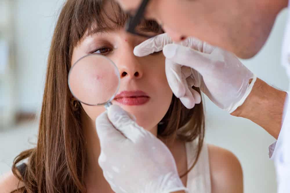 A dermatologist inspects inflammatory acne on a female patient's face.
