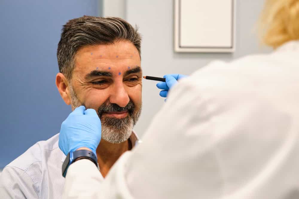 A man getting ready to receive crow’s feet injections from a cosmetic doctor to the outer eye area.
