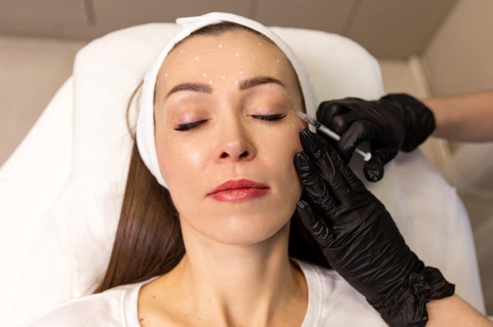 A cosmetic doctor administering Botox for crow's feet to a female patient's outer eye area.